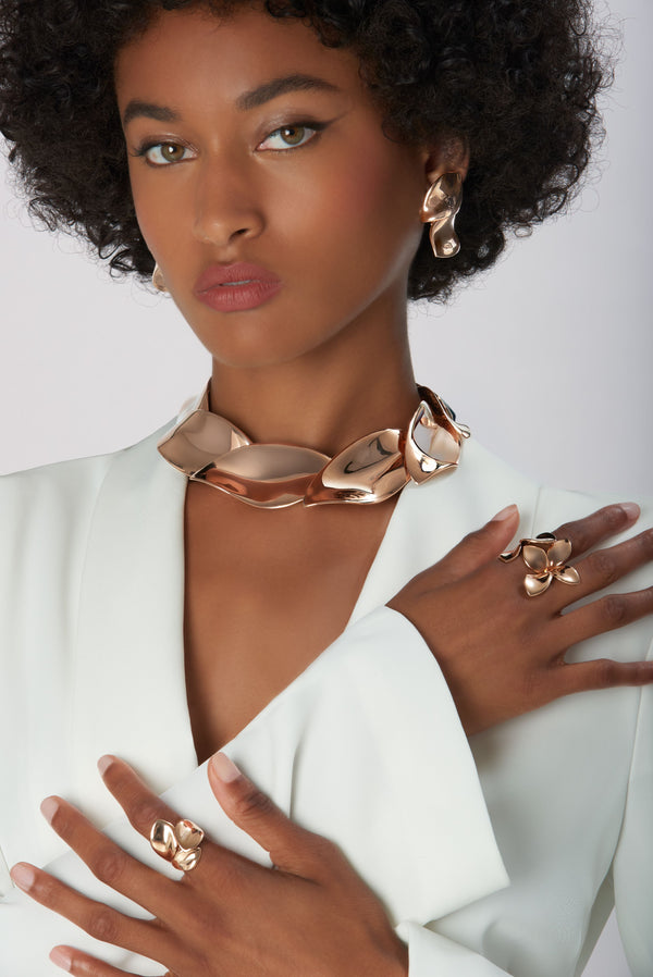 Rings, earrings and necklace in 18k Rose Gold on model wearing a white jacket.