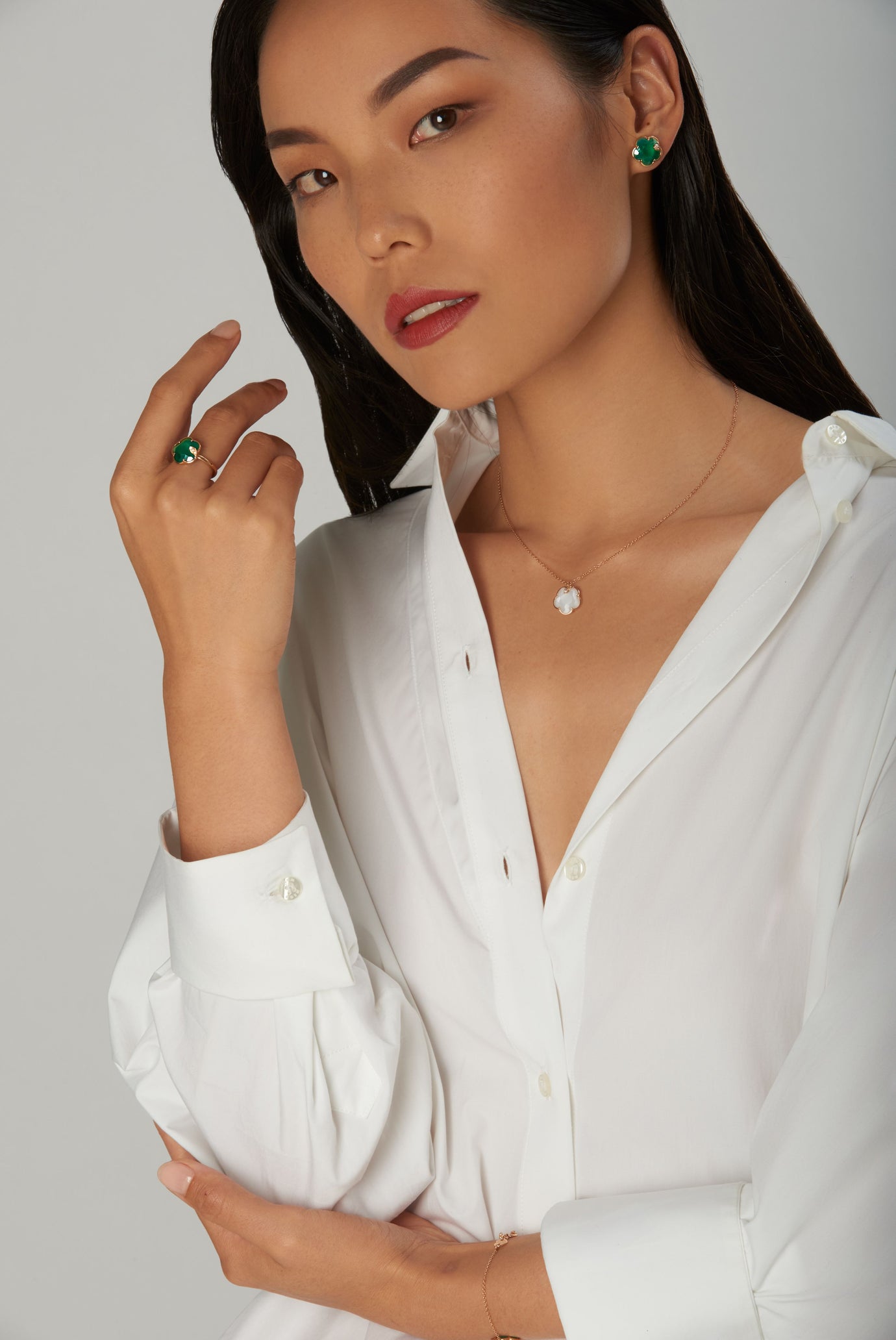 Necklace in 18k rose gold with mother-of-pearl and matching emerald earrings and rings, worn with white shirt