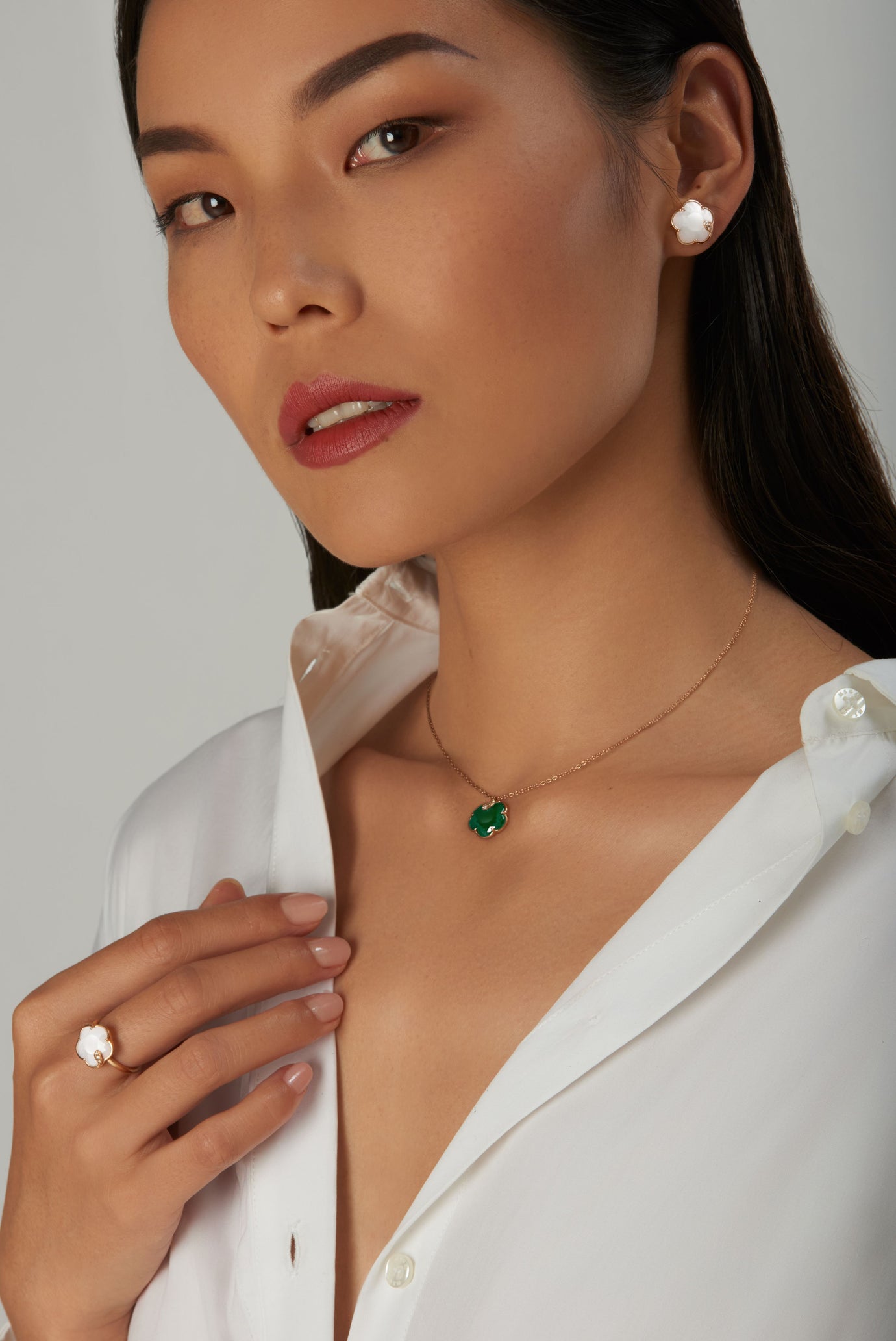 Necklace with emerald and mother-of-pearl earring and ring on model in white shirt