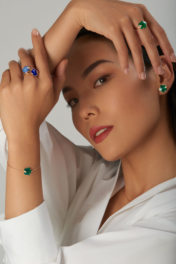 Earrings, rings, and bracelet with green and blue gemstones in 18k rose gold on model in white blouse