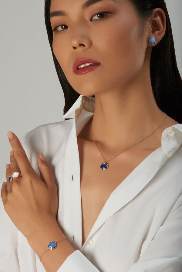 Necklace, earring, bracelet, and ring in 18k rose gold with blue and white gems worn with a white shirt 