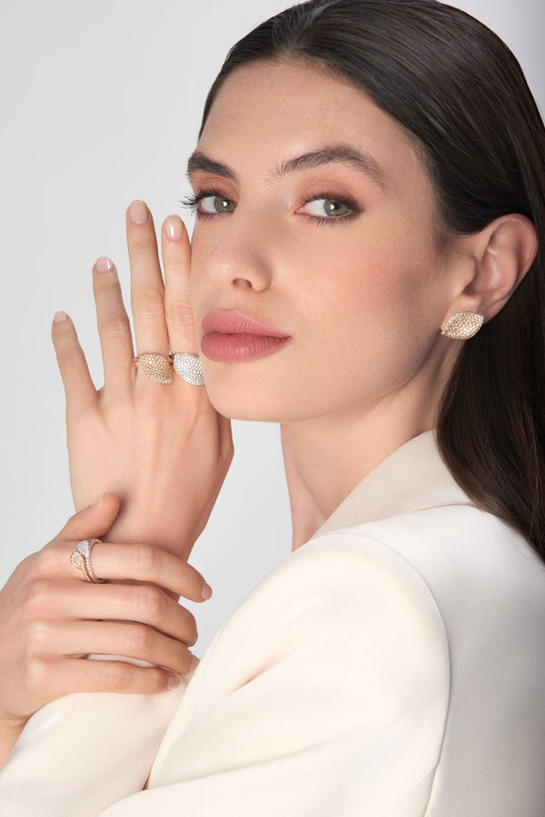 Leaf-shaped earrings and rings in 18k gold and diamonds on a model wearing a cream blaze