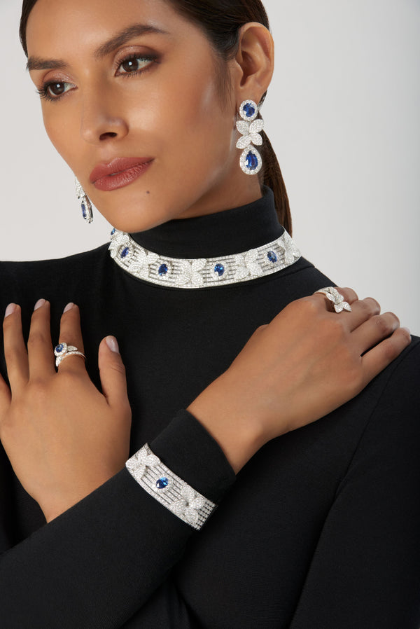 Earrings, choker, ring, and bracelet in 18k white gold with blue sapphires and diamonds on model with a turtleneck