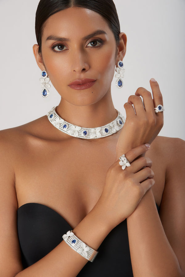 Necklace, earrings, ring, and bracelet in 18k white gold with blue sapphires and diamonds on model in black outfit