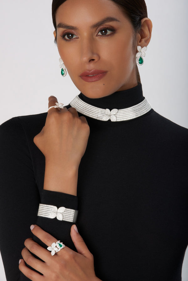 Earrings, choker, bracelet and ring in 18k white gold with emeralds and diamonds on model in black turtleneck