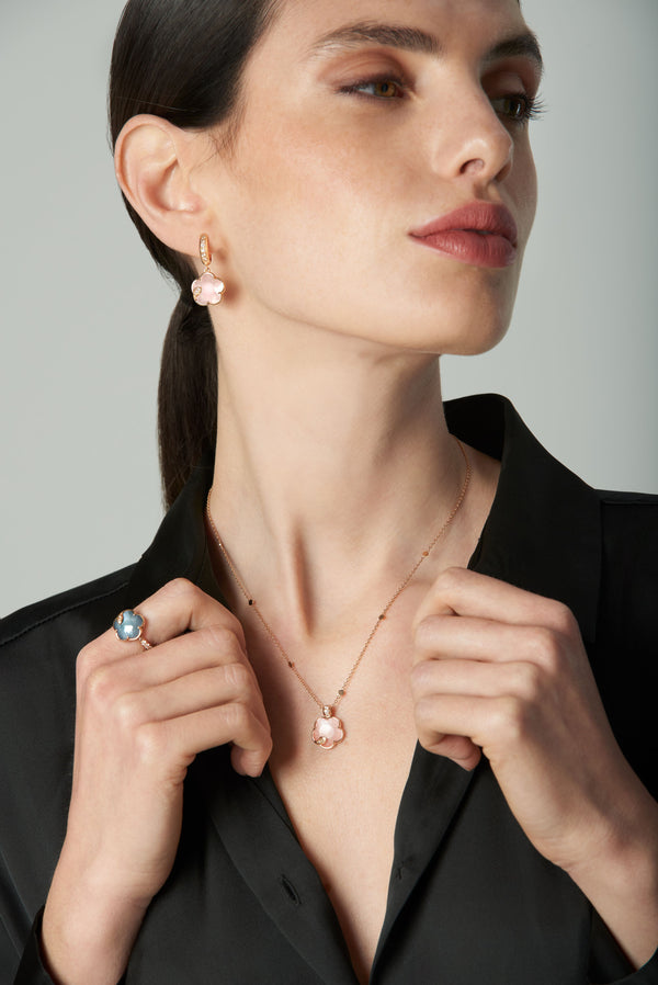 Earrings and necklace in 18k rose gold with pink and blue gemstones and diamonds, worn by model in black shirt