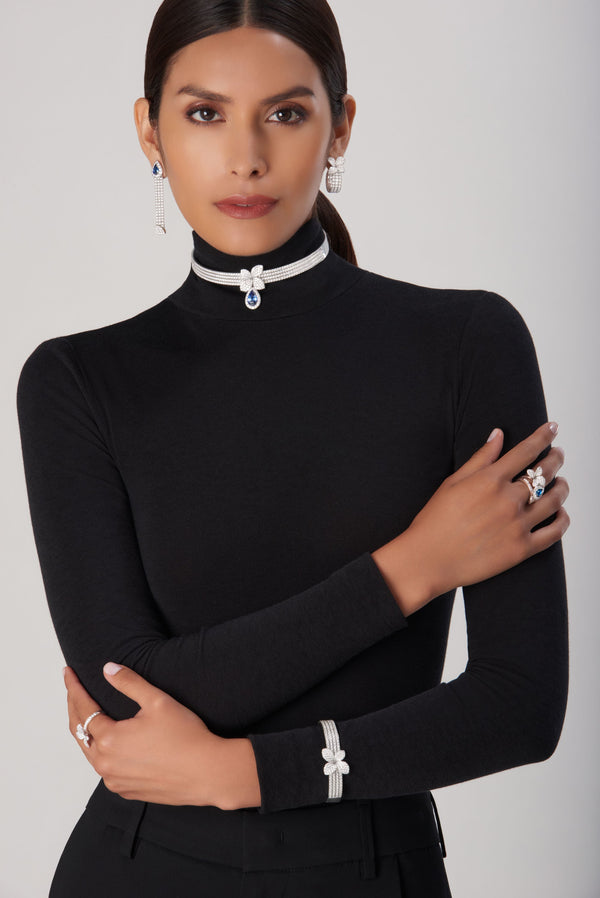 Choker, earrings, and bracelet in 18k white gold with blue sapphires and diamonds on model in turtleneck