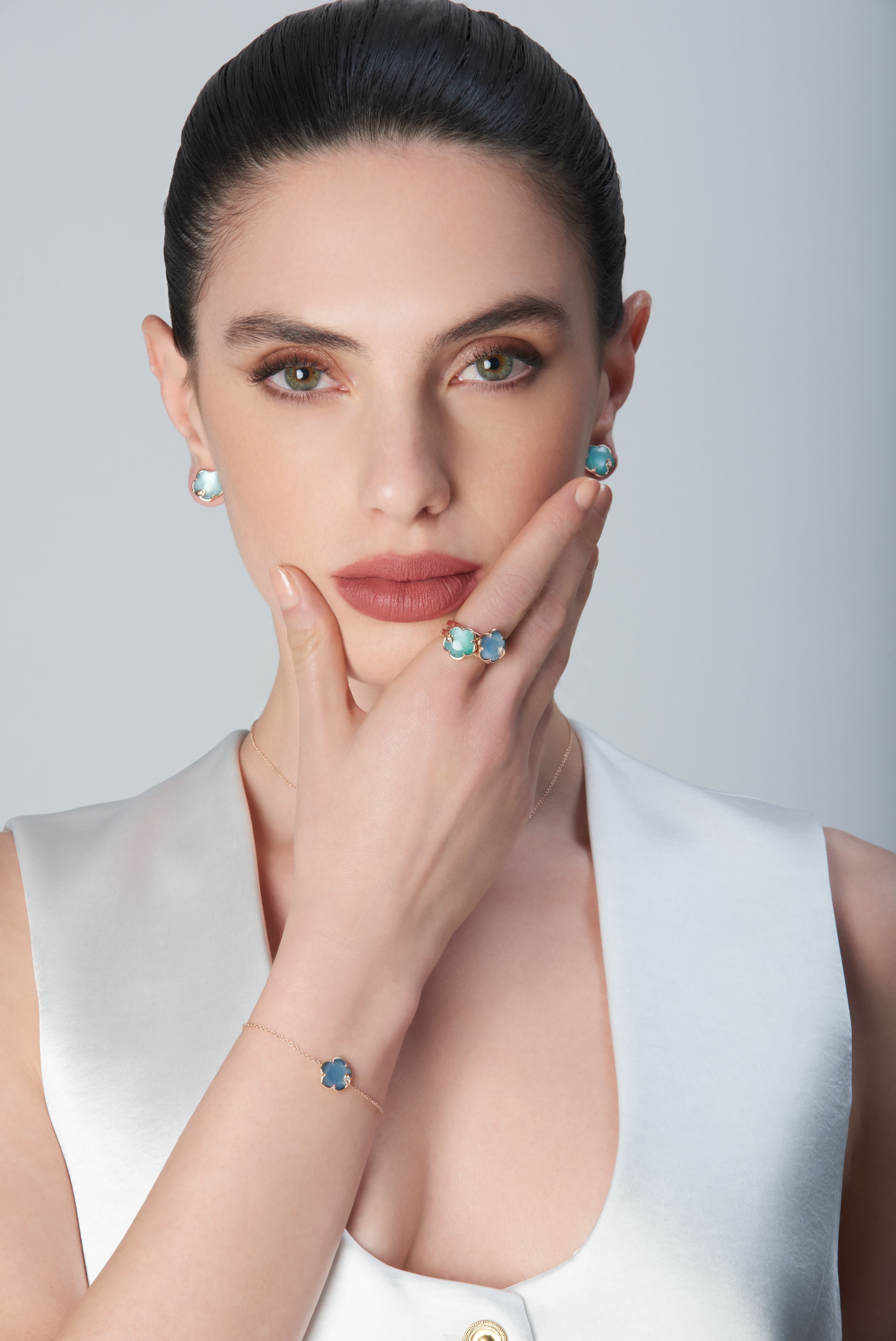 Combination of earrings, rings and bracelet in 18k Rose Gold with coloured gems on model wearing white top