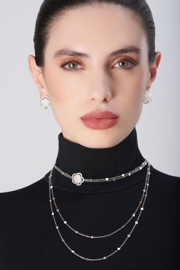 Diamond stud earrings and layered necklace in 18k white gold with floral motifs displayed on model wearing a black turtleneck