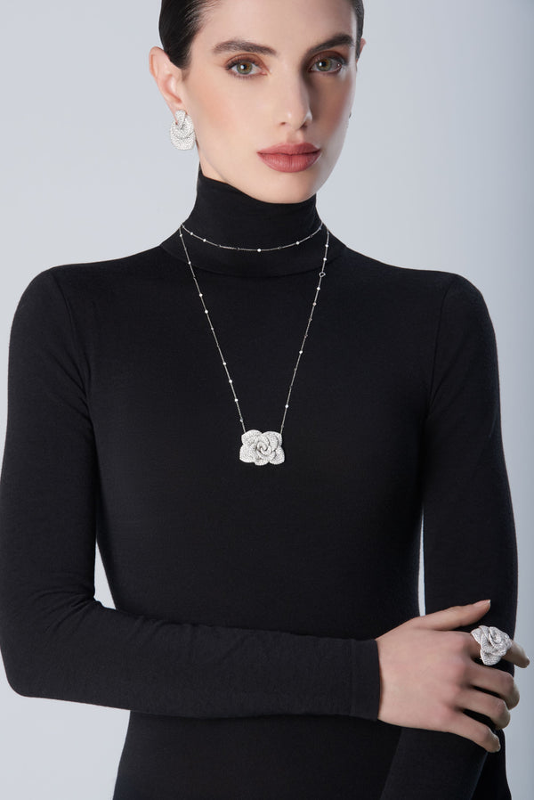 Woman wearing a black turtleneck with 18k white gold set of earrings, necklace and ring
