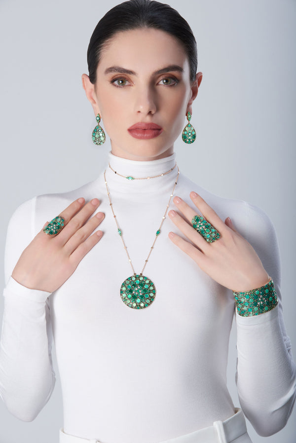 Earrings, necklace, rings and bracelet in in 18k Rose Gold with green precious gemstones on model with a white turtleneck