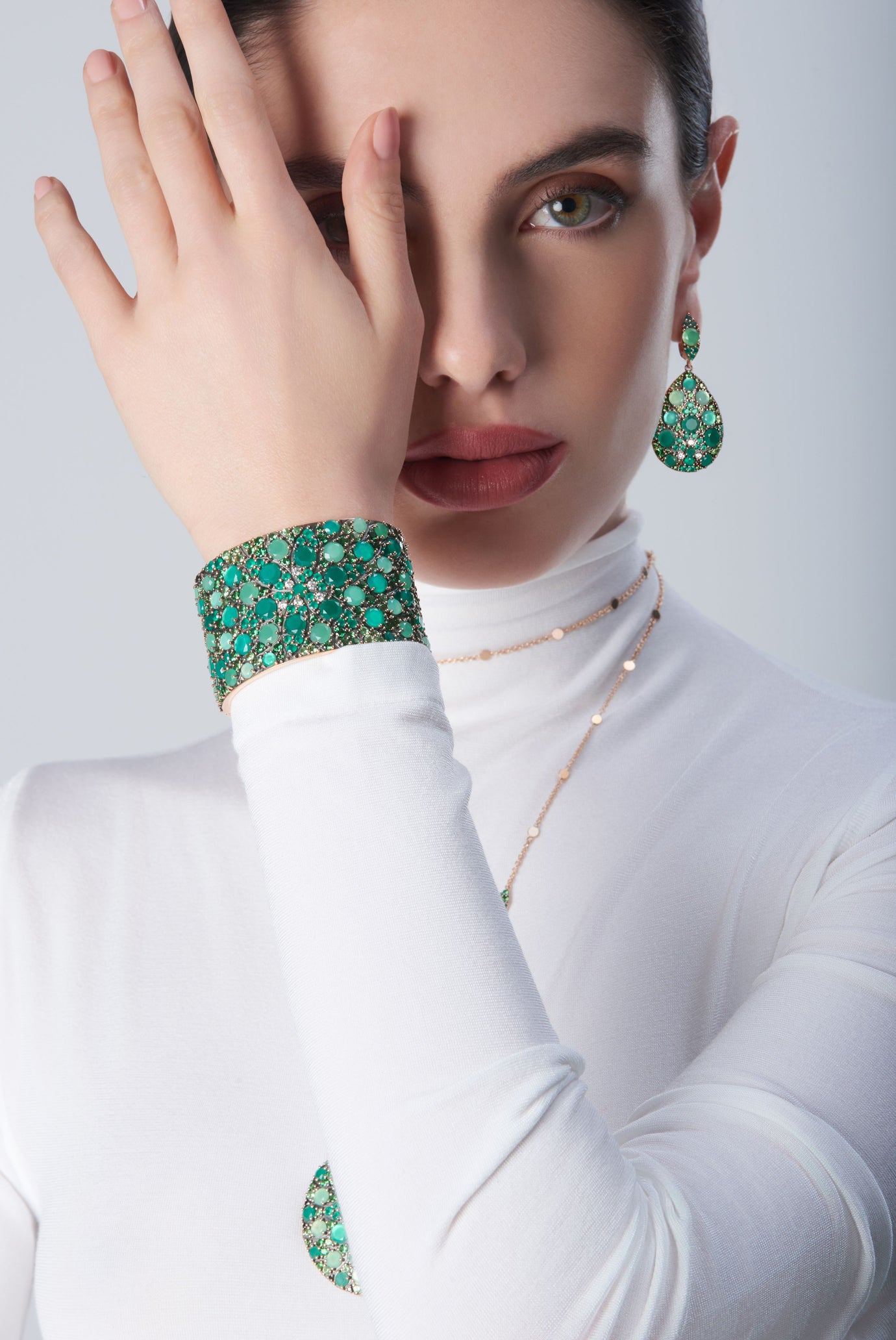Bracelet and earrings in in 18k Rose Gold with green precious gemstones on model with a white look