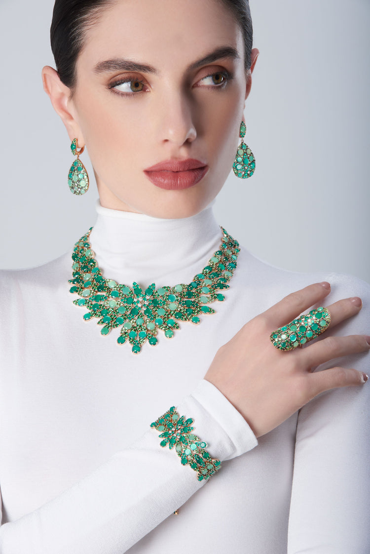 Earrings, collier, bracelet and ring in 18k Rose gold with diamonds and green precious gemstones on a white turtleneck