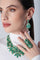 Combination of earrings, necklace and ring in 18k Rose Gold with green precious gemstones on model with a white turtleneck