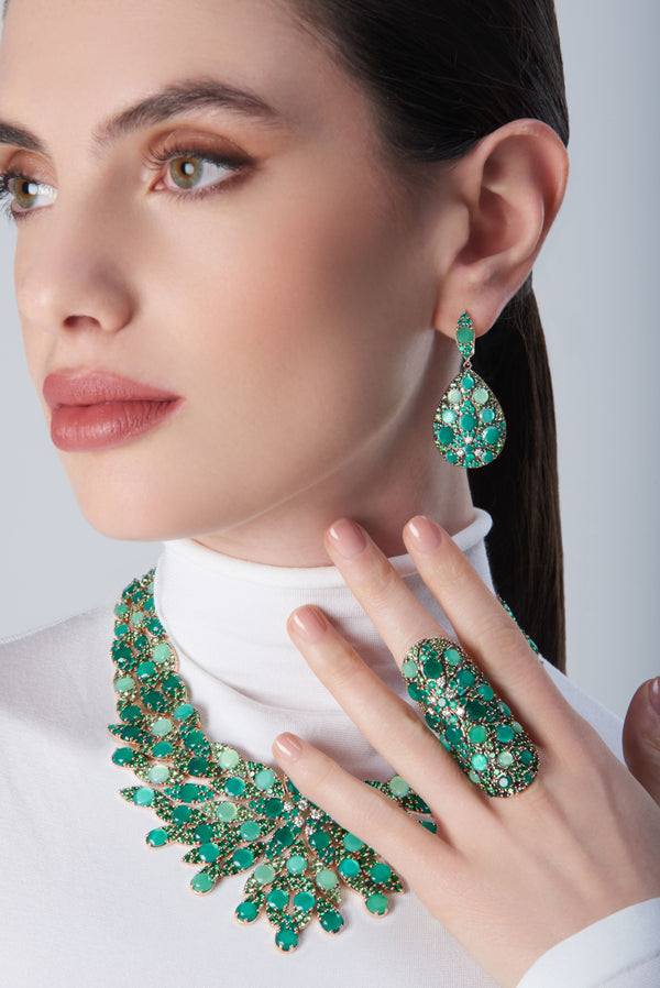 Combination of earrings, necklace and ring in 18k Rose Gold with green precious gemstones on model with a white turtleneck